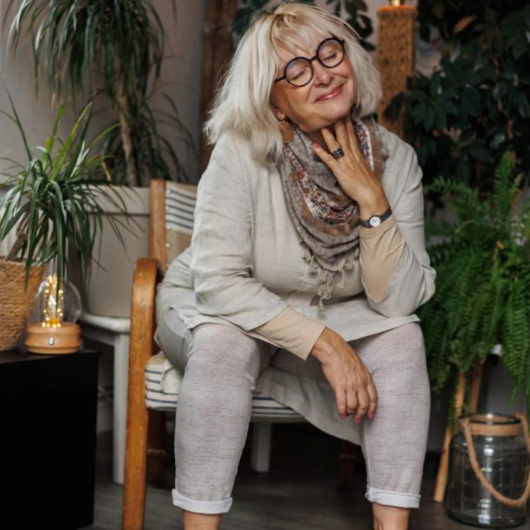 Portrait d'une femme aux cheveux blancs, assise dans un fauteuil entouré de plantes