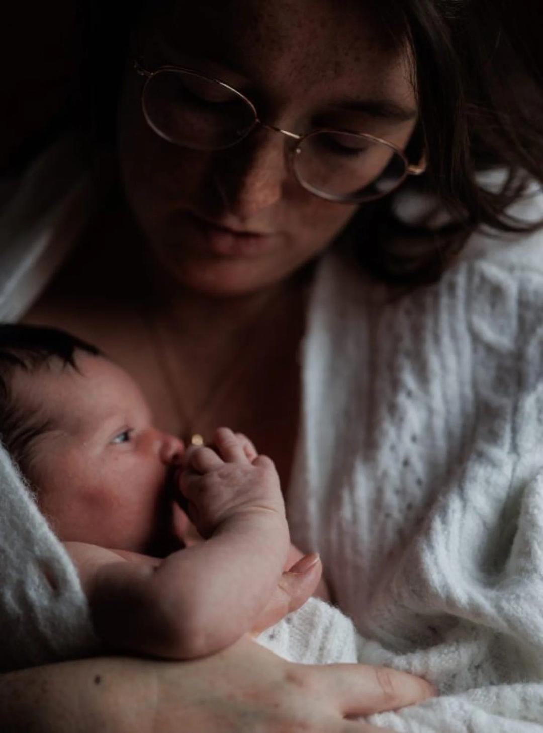 Une jeune maman en gilet blanc tient son nouveau-né contre elle