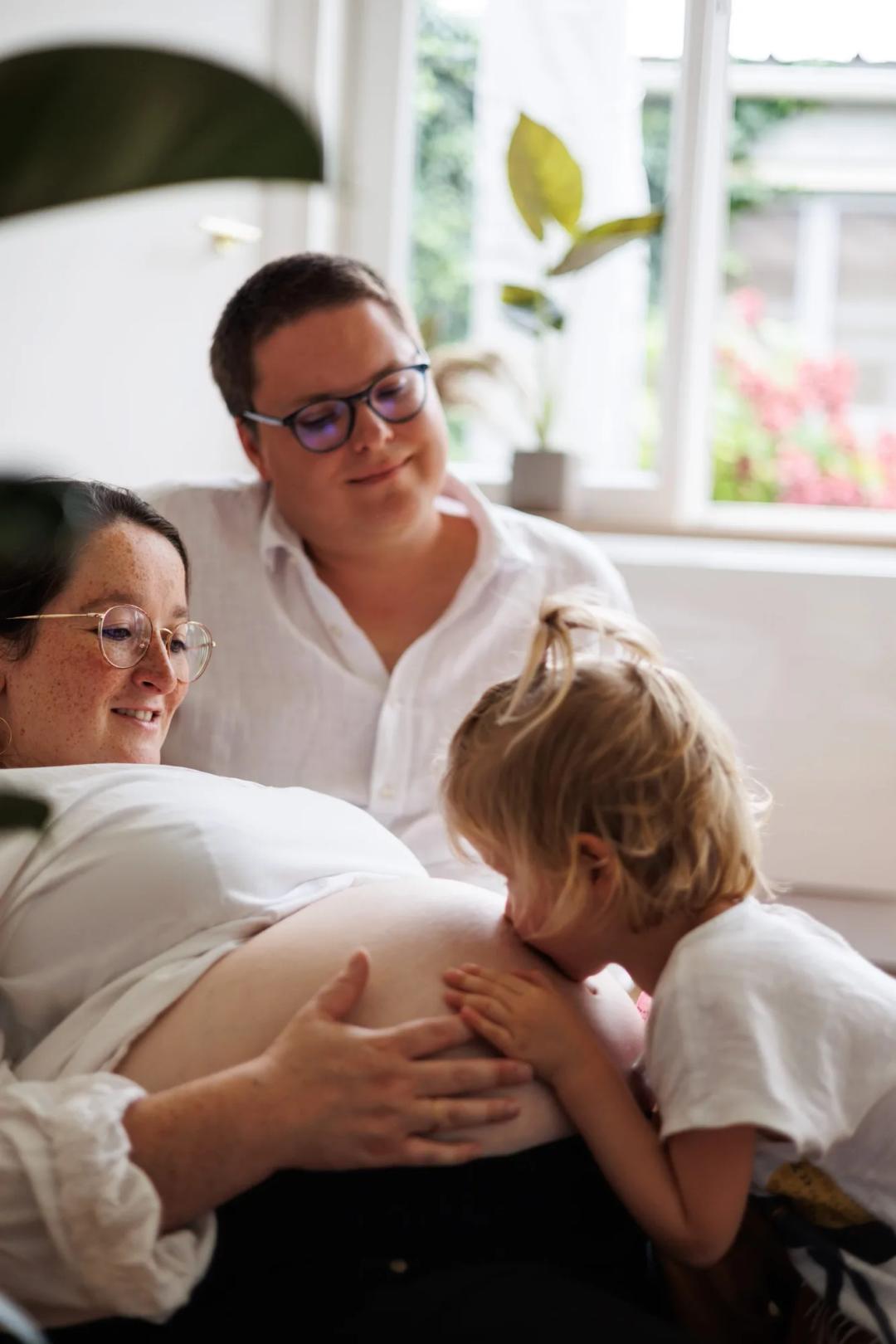 Une petite fille embrasse le ventre rond de sa maman, entourée de sa famille
