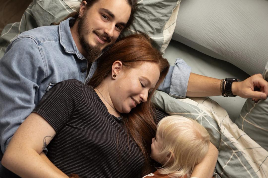 Un couple allongé sur le lit avec leur enfant, sourires complices