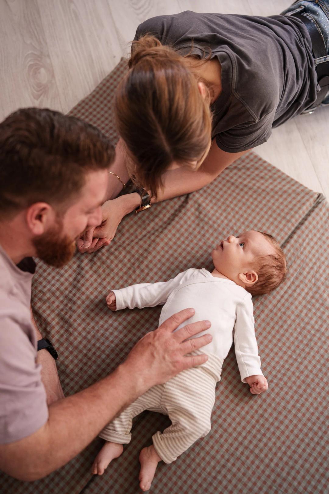 Des parents penchés sur leur bébé, allongé sur une couverture