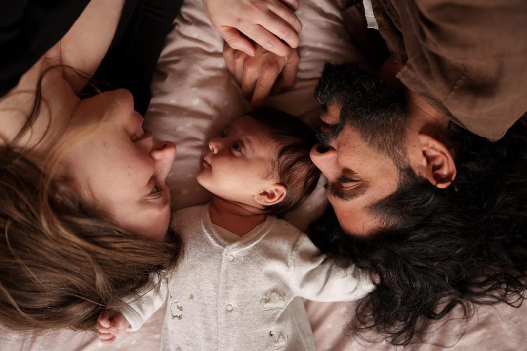 Des parents et leur bébé, têtes rapprochées sur le lit