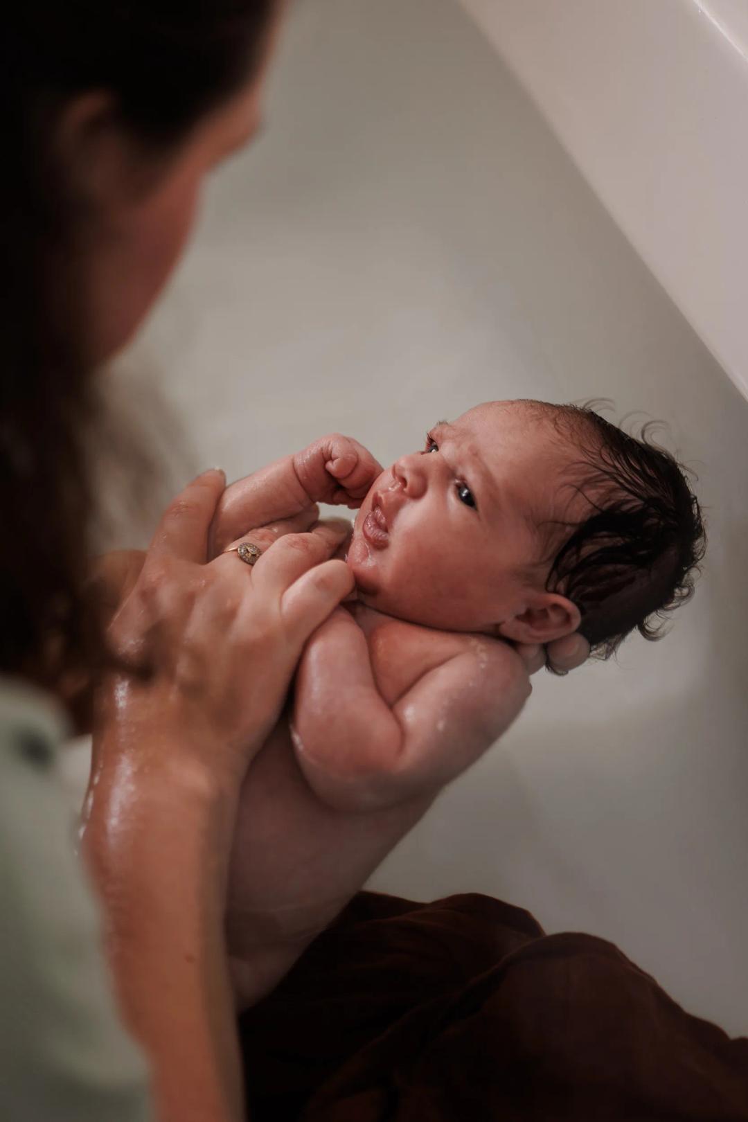 Un nouveau-né dans son bain, soutenu par les mains de sa maman