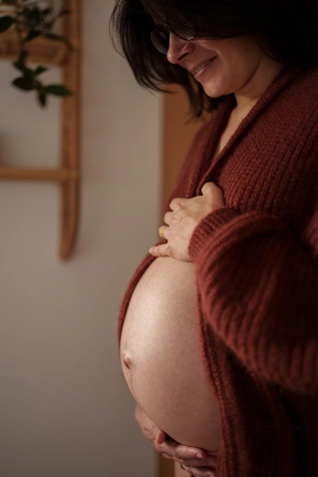 Une future maman en gilet bordeaux, les mains sur son ventre