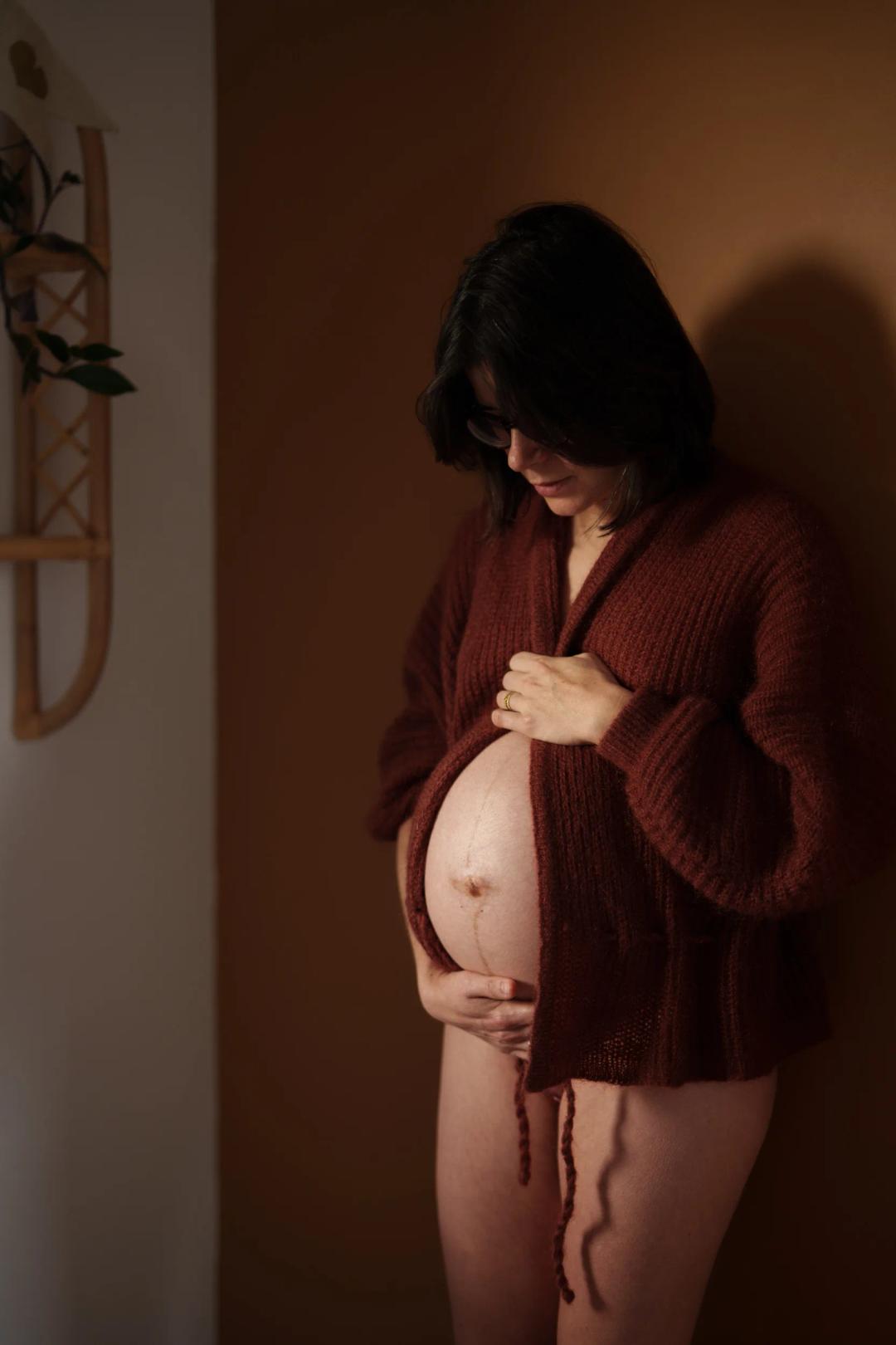 Une femme enceinte, gilet ouvert, les mains sur son ventre