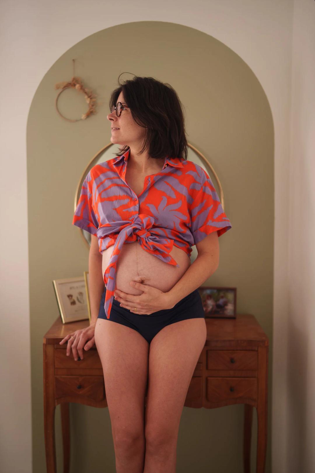 Une future maman en chemise colorée nouée sur le ventre, devant une arche