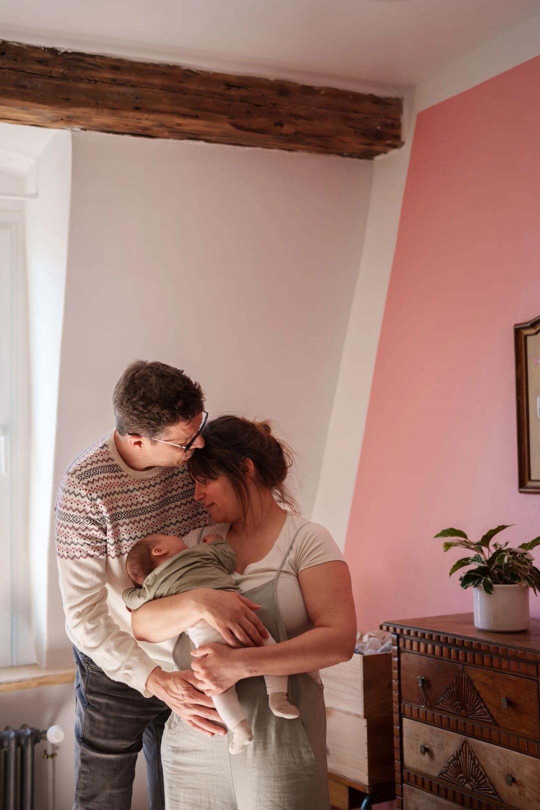 Des parents serrent leur nouveau-né contre eux, dans une chambre au mur rose