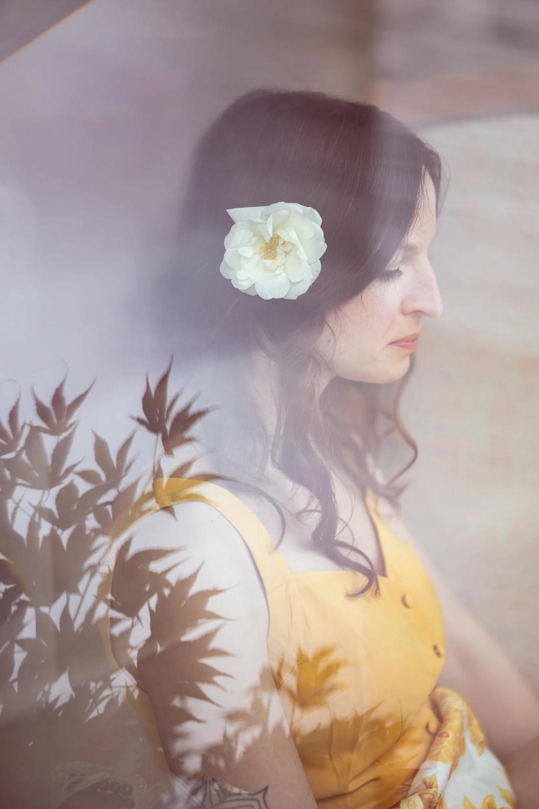 Une femme, une fleur blanche dans les cheveux, regarde par la fenêtre
