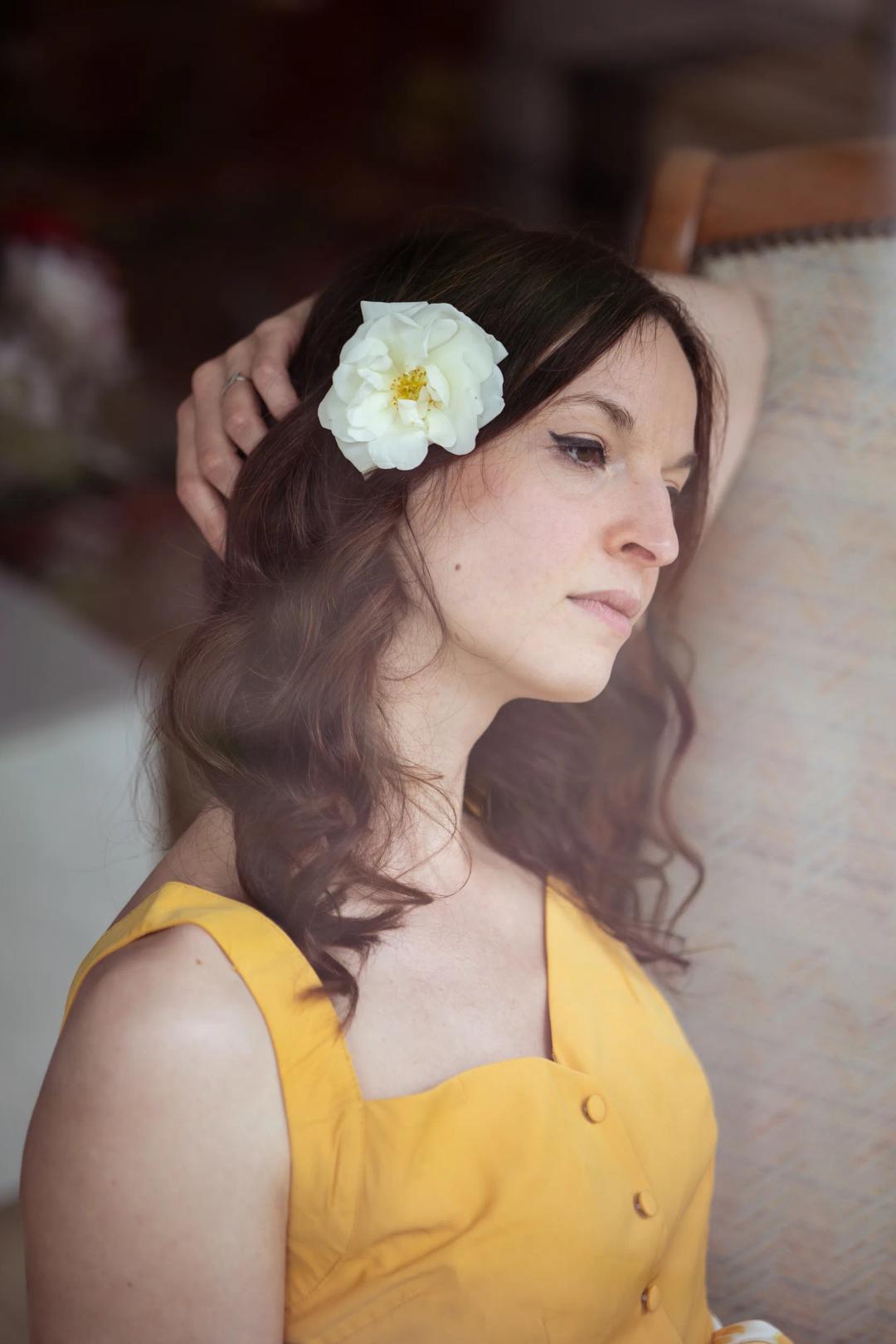 Une femme en robe jaune, une fleur dans les cheveux, le regard au loin