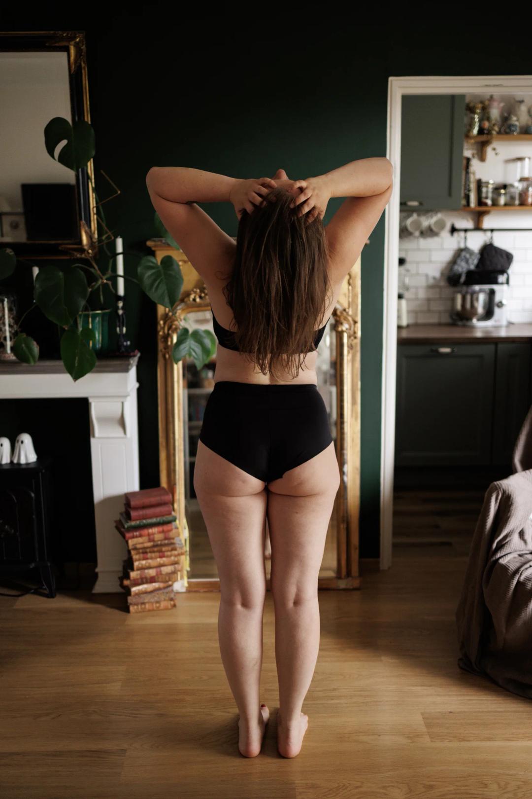 Une femme de dos, les mains dans les cheveux, dans son salon